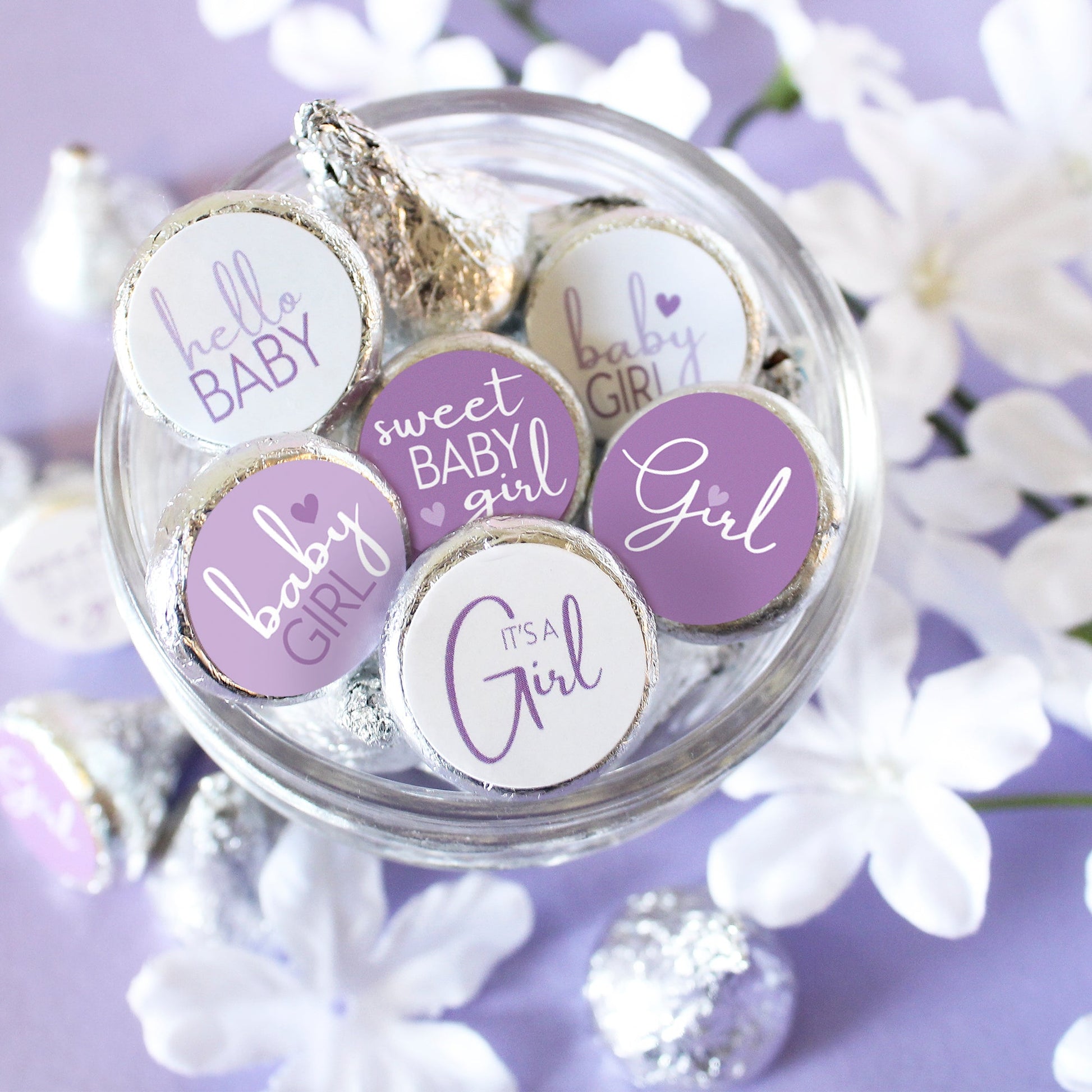 A photo of a jar filled with kisses candies, each one adorned with a purple 'It's a Girl' sticker.